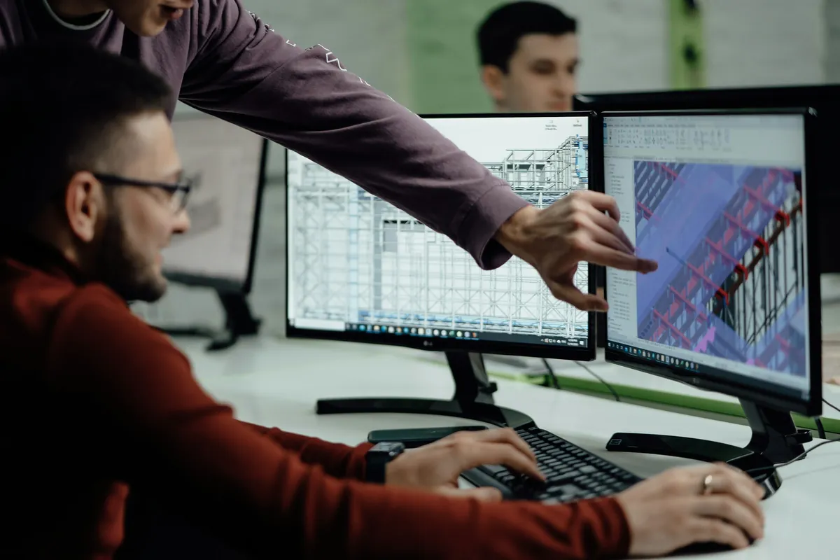 Two engineers reviewing a 3D structural design across a pair of monitors